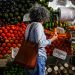 Woman shopping at a vibrant local market stall filled with fresh fruits and vegetables.